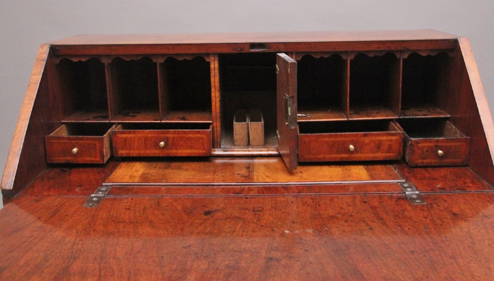 An 18th century walnut writing bureau featuring a sloped fall-front lid, brass drop handles, keyhole escutcheons, and turned ball feet. View IX