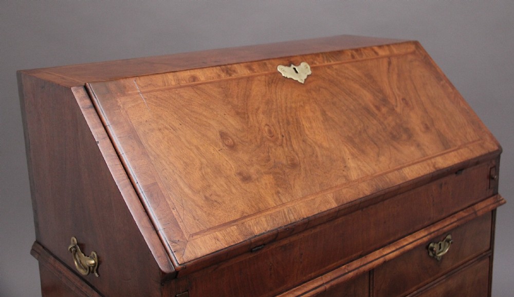 An 18th century walnut writing bureau featuring a sloped fall-front lid, brass drop handles, keyhole escutcheons, and turned ball feet. View X