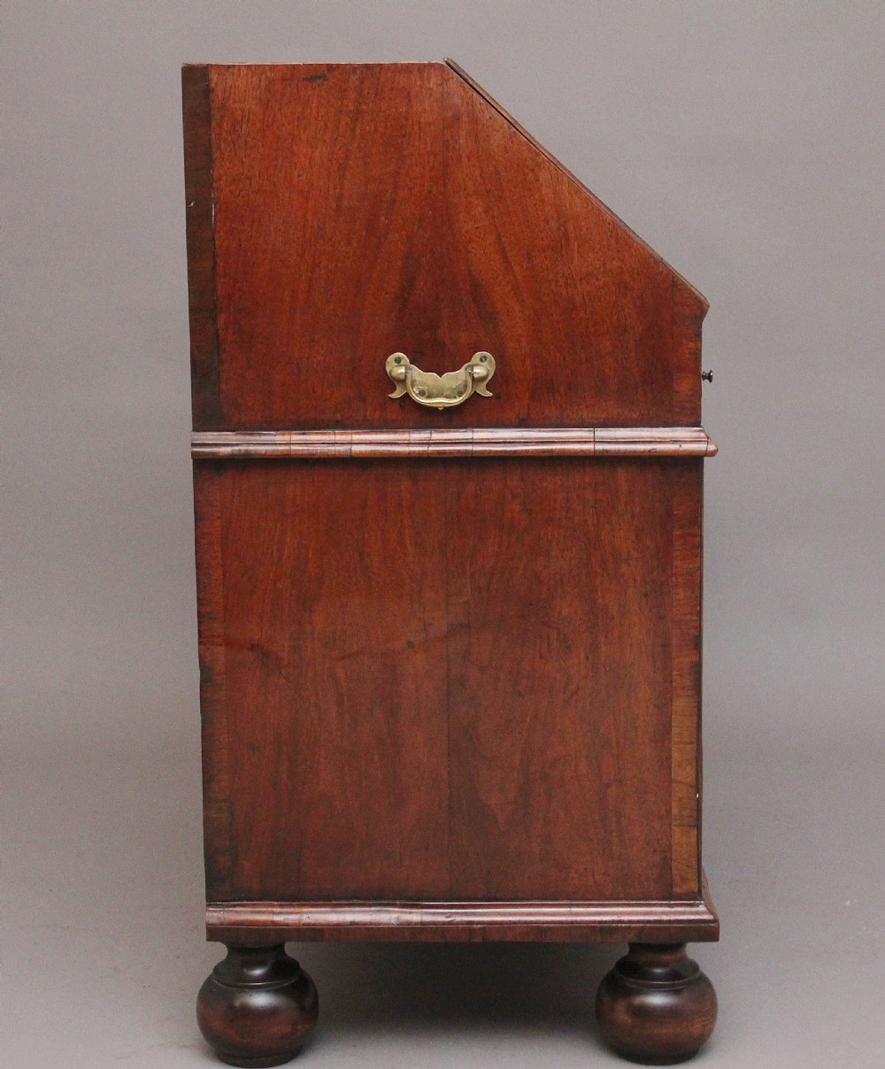 An 18th century walnut writing bureau featuring a sloped fall-front lid, brass drop handles, keyhole escutcheons, and turned ball feet. View XI