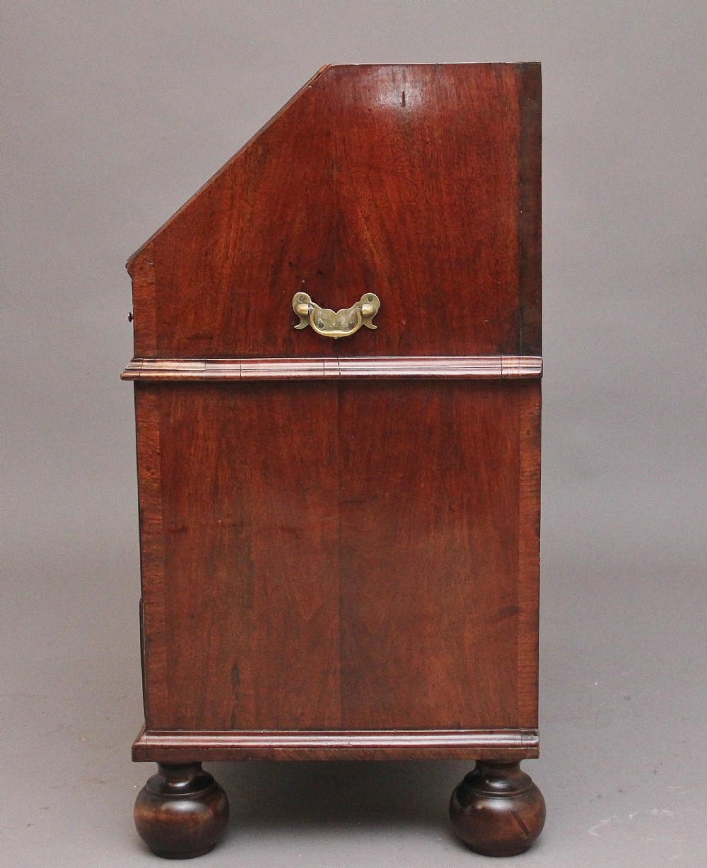 An 18th century walnut writing bureau featuring a sloped fall-front lid, brass drop handles, keyhole escutcheons, and turned ball feet. View XIII