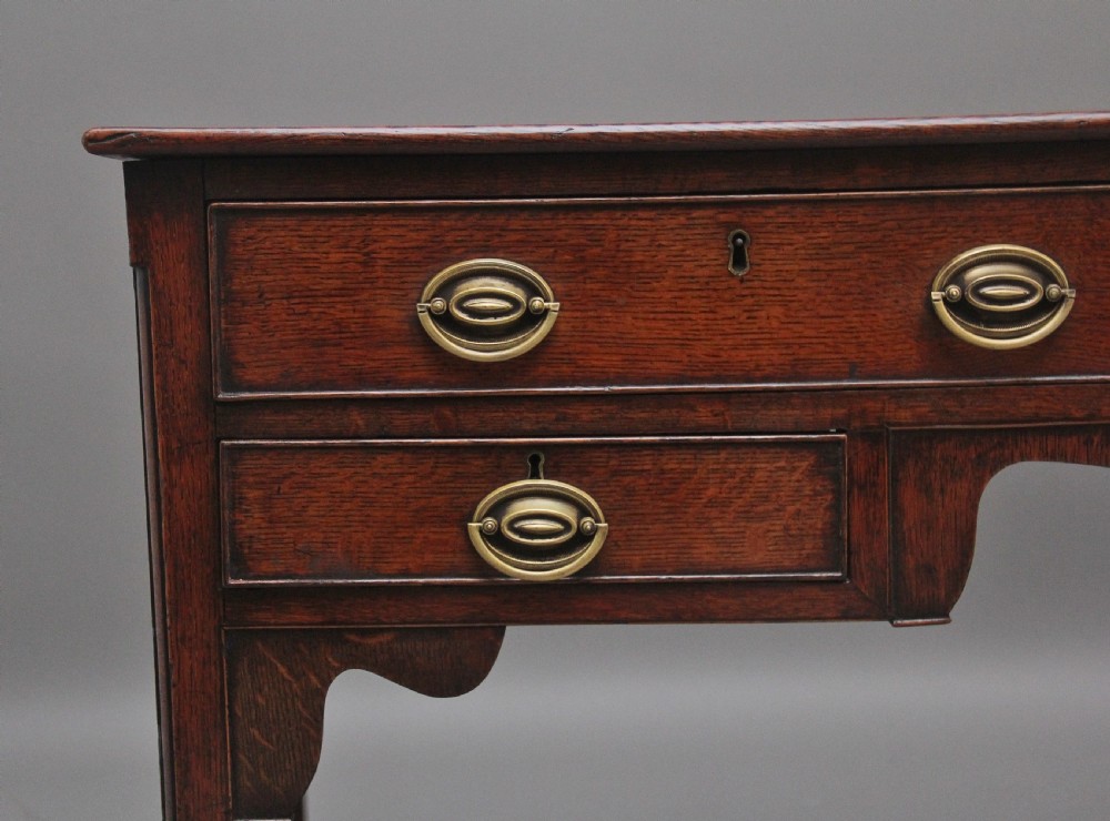 An early 19th-century dark oak dresser base featuring five drawers with brass oval handles, an arched central apron, and a lower potboard shelf. View III