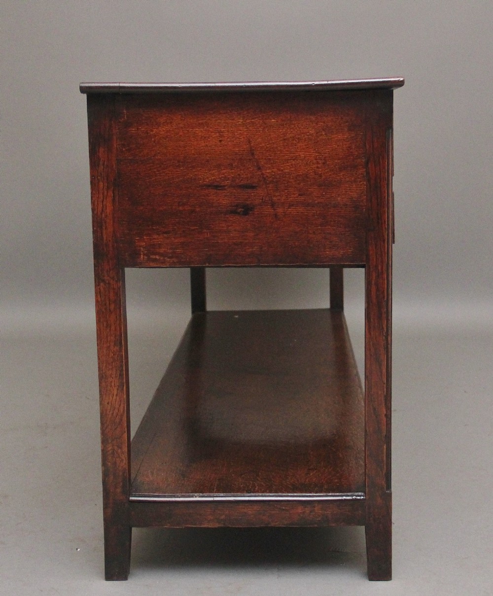 An early 19th-century dark oak dresser base featuring five drawers with brass oval handles, an arched central apron, and a lower potboard shelf. View IV