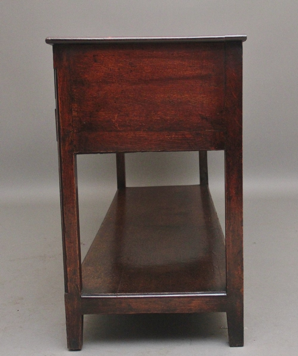 An early 19th-century dark oak dresser base featuring five drawers with brass oval handles, an arched central apron, and a lower potboard shelf. View V