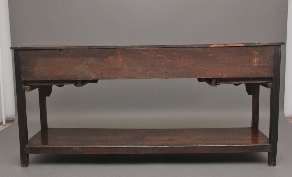 An early 19th-century dark oak dresser base featuring five drawers with brass oval handles, an arched central apron, and a lower potboard shelf. View VI