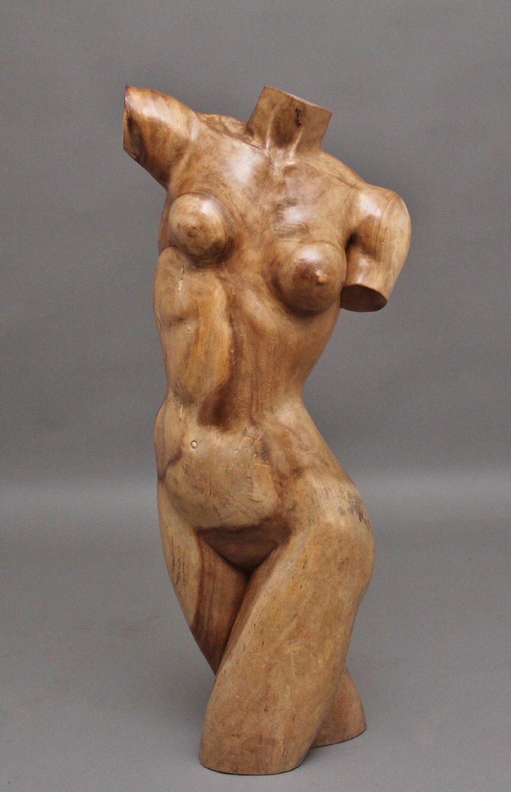 A life-size carved wooden female torso sculpture displayed against a neutral grey background.