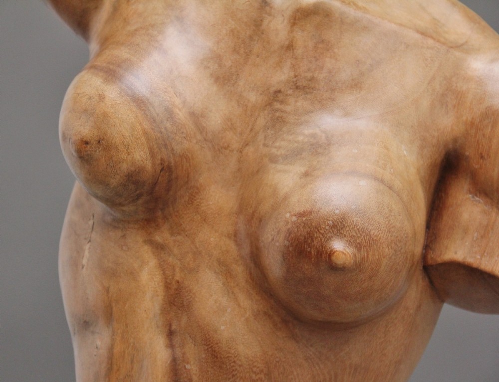 A life-size carved wooden female torso sculpture displayed against a neutral grey background. View X