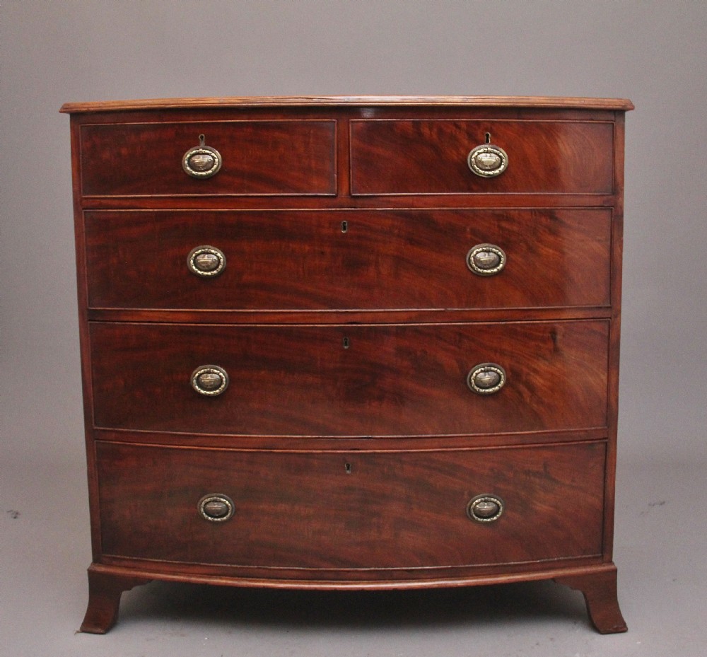 An early nineteenth-century mahogany bowfront chest of drawers featuring two short drawers over three long drawers with brass oval handles and bracket feet.