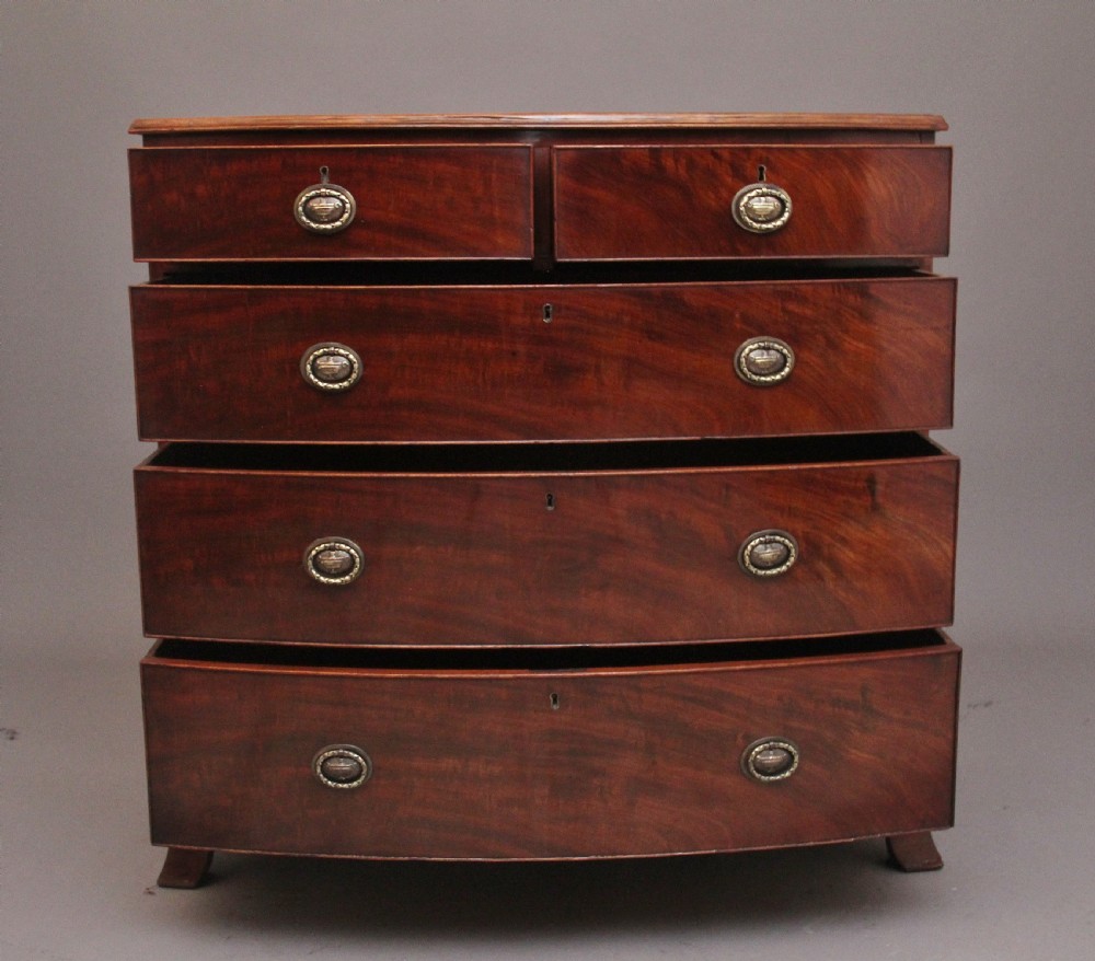 An early nineteenth-century mahogany bowfront chest of drawers featuring two short drawers over three long drawers with brass oval handles and bracket feet. View IV