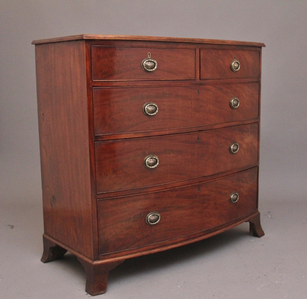 An early nineteenth-century mahogany bowfront chest of drawers featuring two short drawers over three long drawers with brass oval handles and bracket feet. View V
