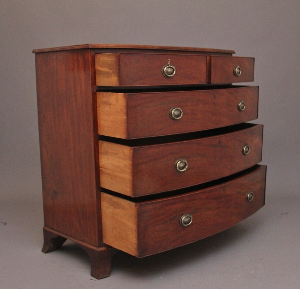 An early nineteenth-century mahogany bowfront chest of drawers featuring two short drawers over three long drawers with brass oval handles and bracket feet. View VII