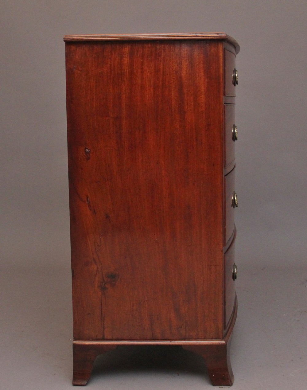 An early nineteenth-century mahogany bowfront chest of drawers featuring two short drawers over three long drawers with brass oval handles and bracket feet. View VIII