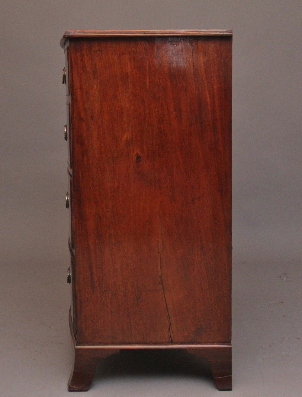 An early nineteenth-century mahogany bowfront chest of drawers featuring two short drawers over three long drawers with brass oval handles and bracket feet. View IX