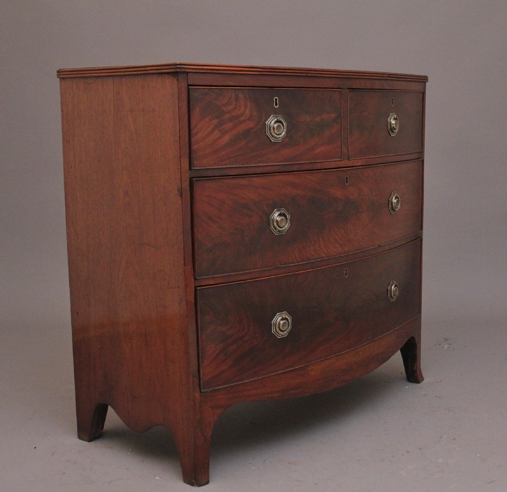 An early nineteenth-century flame mahogany bowfront chest of drawers featuring a two over two drawer configuration with brass octagonal ring handles. View V