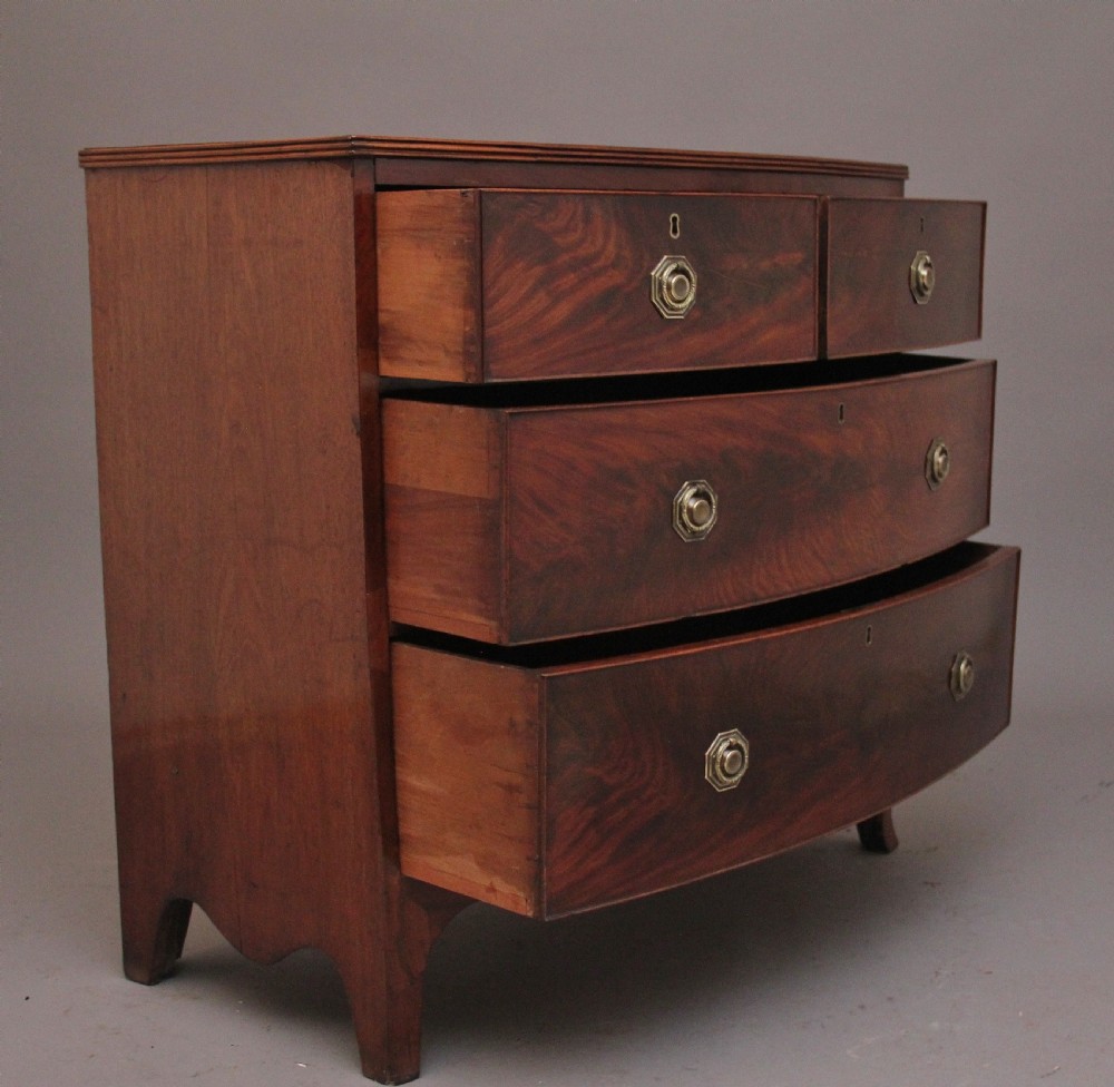 An early nineteenth-century flame mahogany bowfront chest of drawers featuring a two over two drawer configuration with brass octagonal ring handles. View VI