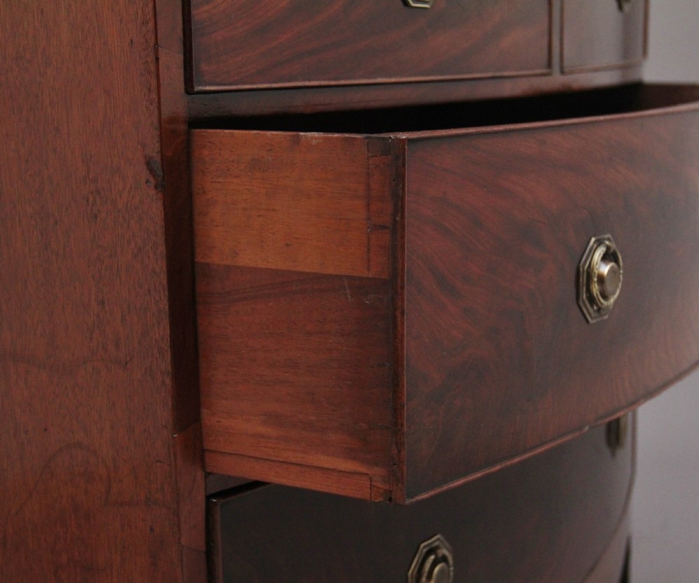 An early nineteenth-century flame mahogany bowfront chest of drawers featuring a two over two drawer configuration with brass octagonal ring handles. View VII