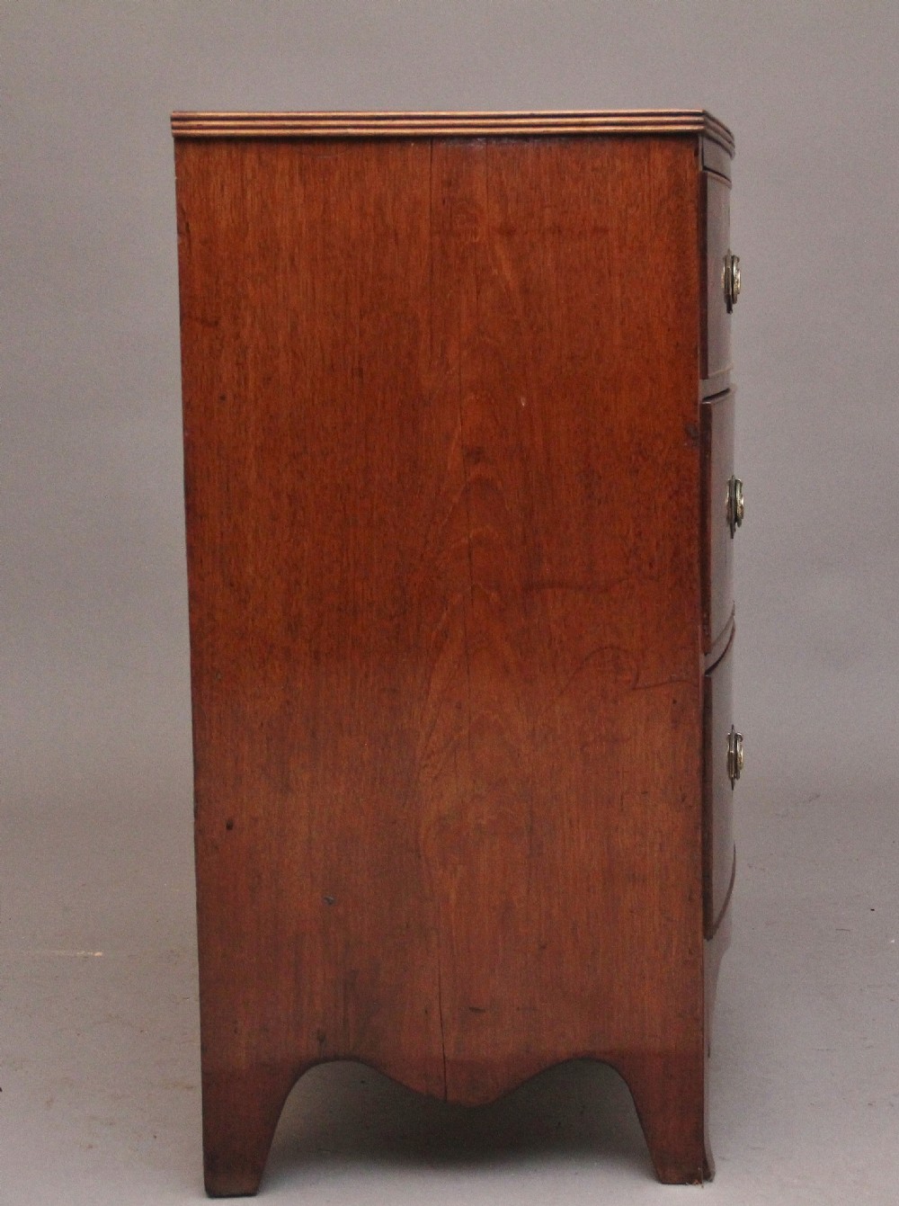 An early nineteenth-century flame mahogany bowfront chest of drawers featuring a two over two drawer configuration with brass octagonal ring handles. View VIII