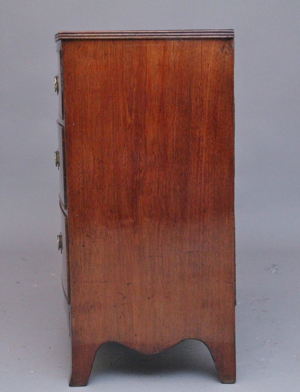An early nineteenth-century flame mahogany bowfront chest of drawers featuring a two over two drawer configuration with brass octagonal ring handles. View X