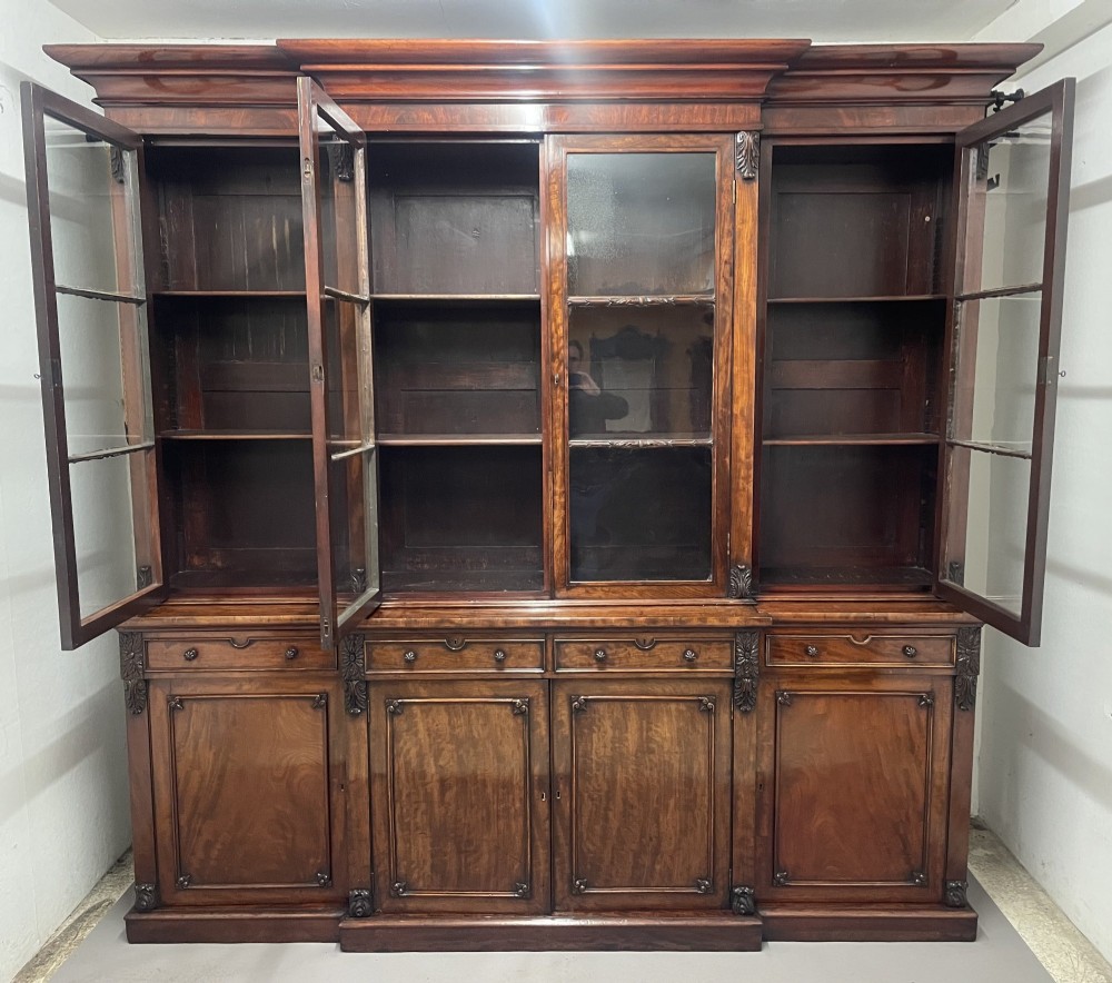 An early 19th-century dark mahogany breakfront bookcase featuring a four-door glazed upper section above four cupboard doors and drawers. View II