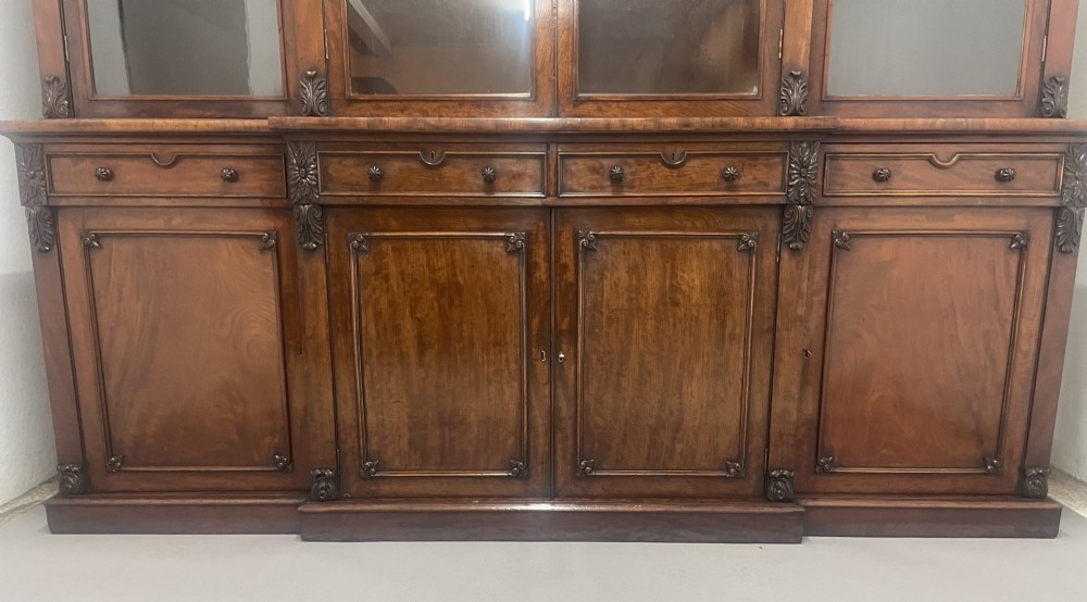 An early 19th-century dark mahogany breakfront bookcase featuring a four-door glazed upper section above four cupboard doors and drawers. View III