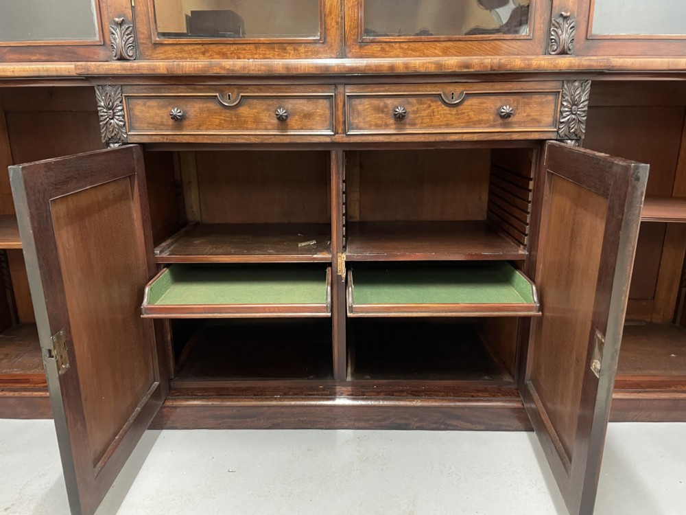 An early 19th-century dark mahogany breakfront bookcase featuring a four-door glazed upper section above four cupboard doors and drawers. View V