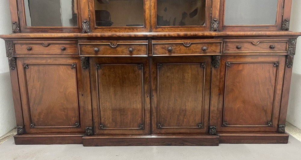 An early 19th-century dark mahogany breakfront bookcase featuring a four-door glazed upper section above four cupboard doors and drawers. View VI