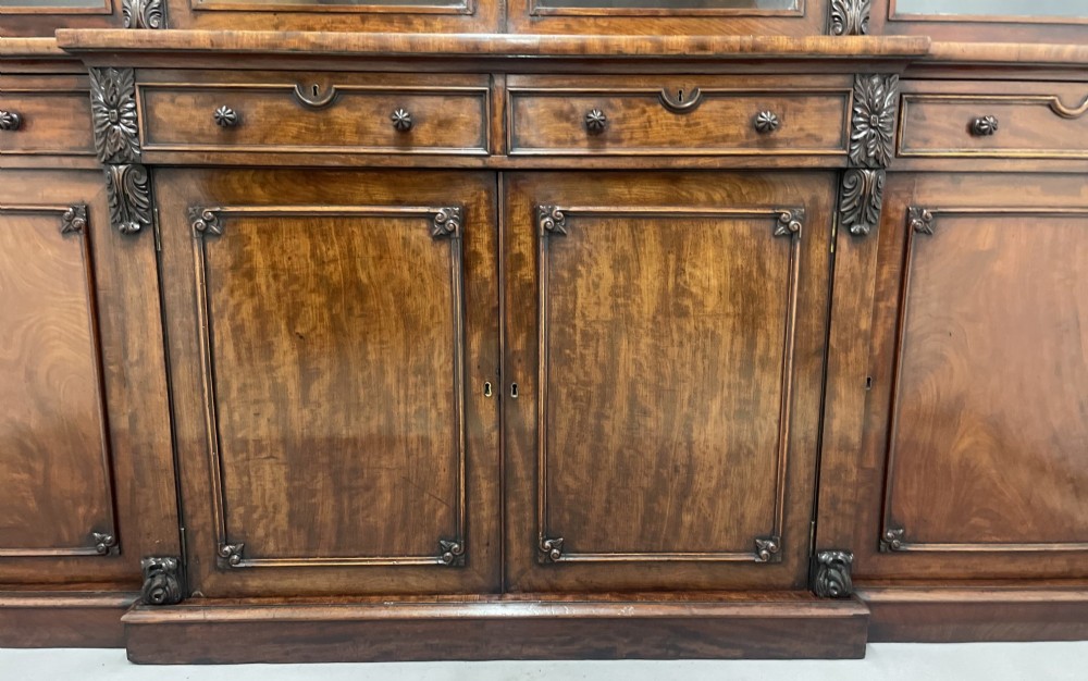 An early 19th-century dark mahogany breakfront bookcase featuring a four-door glazed upper section above four cupboard doors and drawers. View VIII