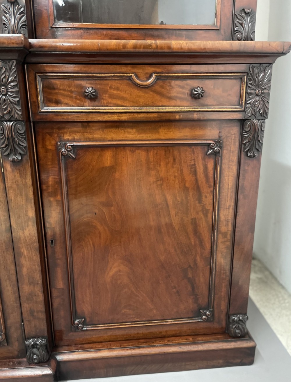 An early 19th-century dark mahogany breakfront bookcase featuring a four-door glazed upper section above four cupboard doors and drawers. View IX