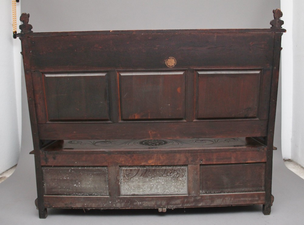 A 19th-century dark oak box settle with intricate relief-carved narrative panels, carved lion head armrests, and a hinged seat for internal storage. View IV