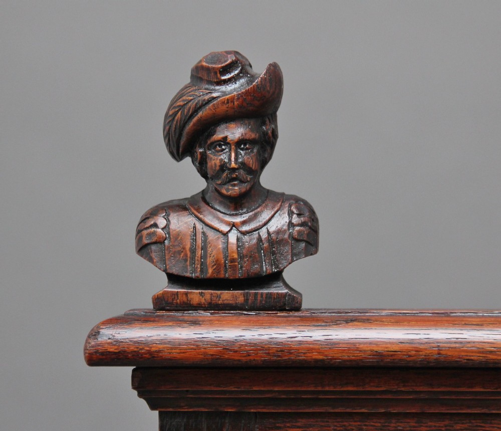 A 19th-century dark oak box settle with intricate relief-carved narrative panels, carved lion head armrests, and a hinged seat for internal storage. View XI