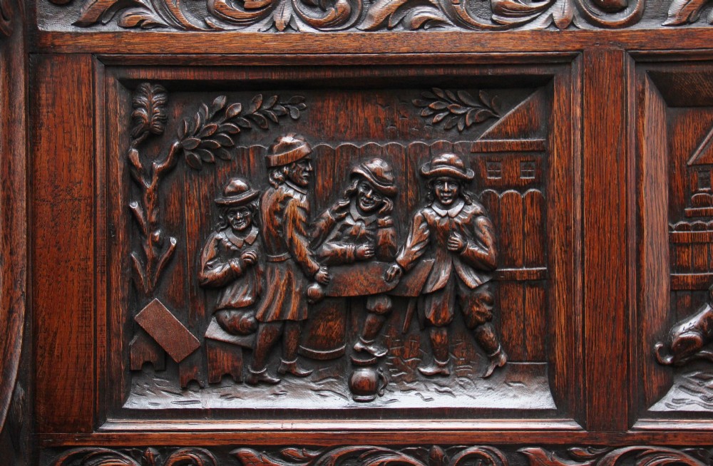 A 19th-century dark oak box settle with intricate relief-carved narrative panels, carved lion head armrests, and a hinged seat for internal storage. View XII