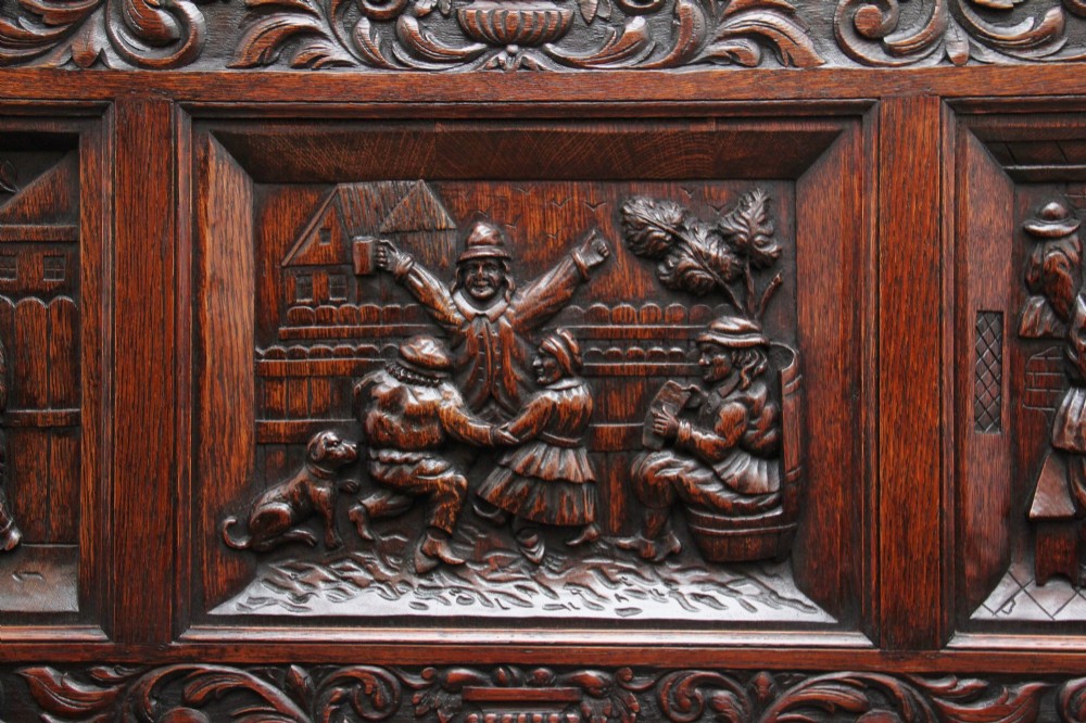 A 19th-century dark oak box settle with intricate relief-carved narrative panels, carved lion head armrests, and a hinged seat for internal storage. View XIII
