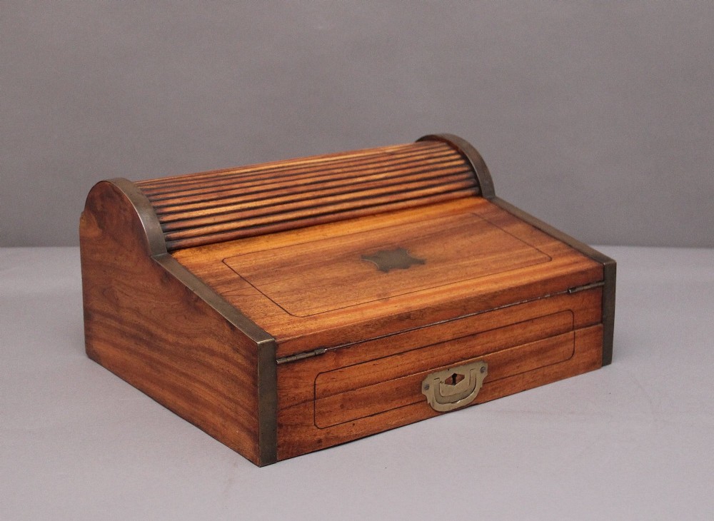 A 19th-century camphor wood writing slope featuring brass-bound corners, a sloped front, a tambour roll-top section, and a central brass inlay plate.