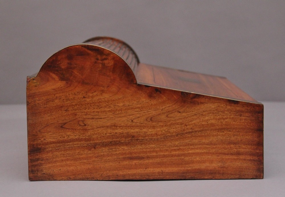 A 19th-century camphor wood writing slope featuring brass-bound corners, a sloped front, a tambour roll-top section, and a central brass inlay plate. View IV