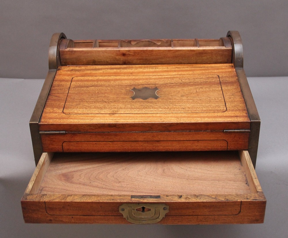 A 19th-century camphor wood writing slope featuring brass-bound corners, a sloped front, a tambour roll-top section, and a central brass inlay plate. View V