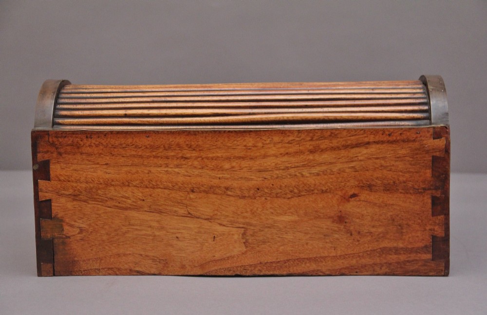 A 19th-century camphor wood writing slope featuring brass-bound corners, a sloped front, a tambour roll-top section, and a central brass inlay plate. View VI