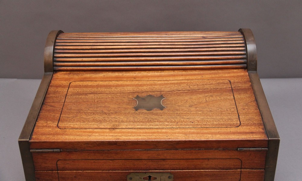 A 19th-century camphor wood writing slope featuring brass-bound corners, a sloped front, a tambour roll-top section, and a central brass inlay plate. View VII