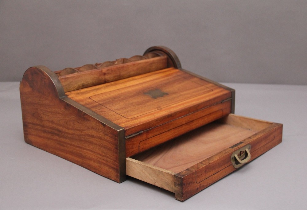 A 19th-century camphor wood writing slope featuring brass-bound corners, a sloped front, a tambour roll-top section, and a central brass inlay plate. View IX
