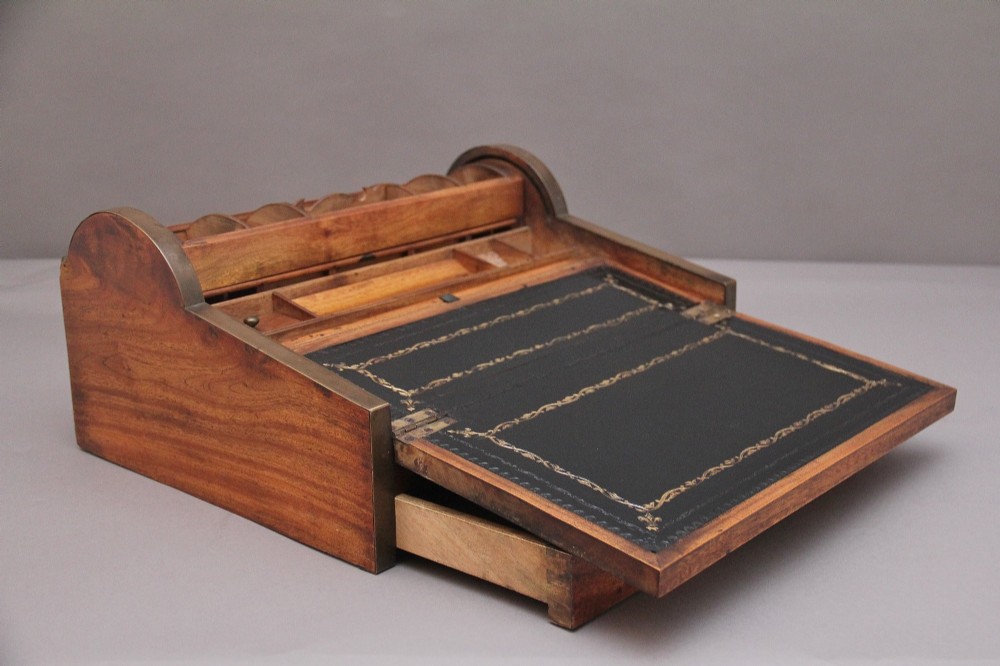 A 19th-century camphor wood writing slope featuring brass-bound corners, a sloped front, a tambour roll-top section, and a central brass inlay plate. View X