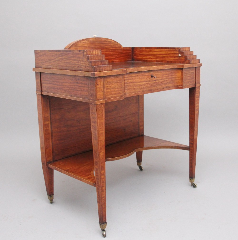 A 19th-century satinwood ladies writing table featuring a stepped side gallery, single frieze drawer, tapered square legs on brass castors, and a lower undertier.