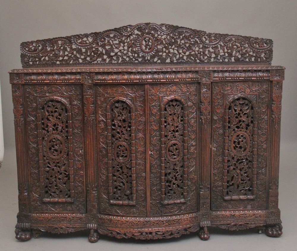 A 19th-century Anglo-Indian dark wood cabinet featuring elaborate pierced foliage carvings, four cupboard doors, and a decorative carved gallery back.