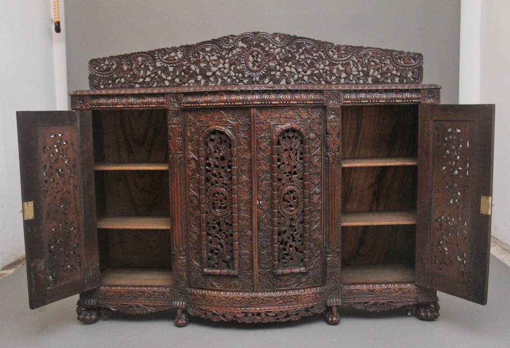 A 19th-century Anglo-Indian dark wood cabinet featuring elaborate pierced foliage carvings, four cupboard doors, and a decorative carved gallery back. View II