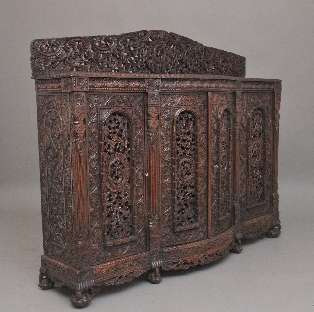 A 19th-century Anglo-Indian dark wood cabinet featuring elaborate pierced foliage carvings, four cupboard doors, and a decorative carved gallery back. View V