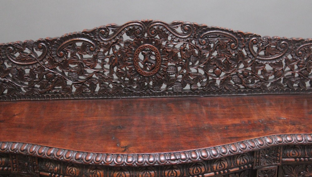 A 19th-century Anglo-Indian dark wood cabinet featuring elaborate pierced foliage carvings, four cupboard doors, and a decorative carved gallery back. View VII