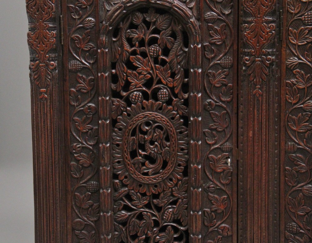 A 19th-century Anglo-Indian dark wood cabinet featuring elaborate pierced foliage carvings, four cupboard doors, and a decorative carved gallery back. View XIII