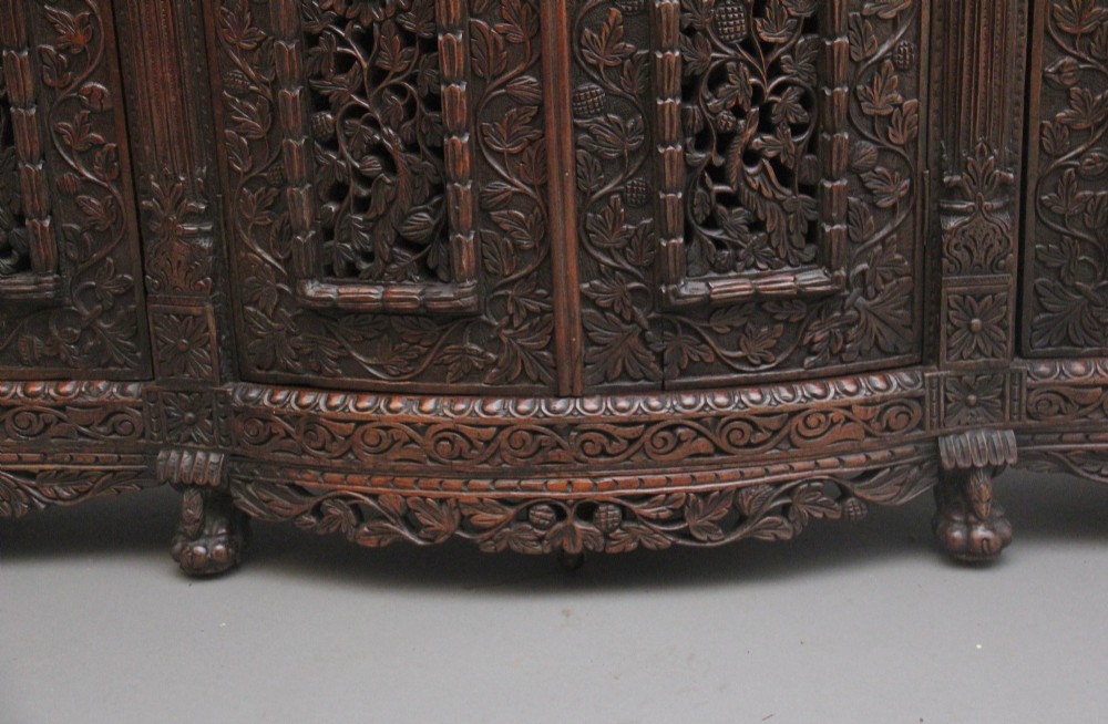 A 19th-century Anglo-Indian dark wood cabinet featuring elaborate pierced foliage carvings, four cupboard doors, and a decorative carved gallery back. View XV