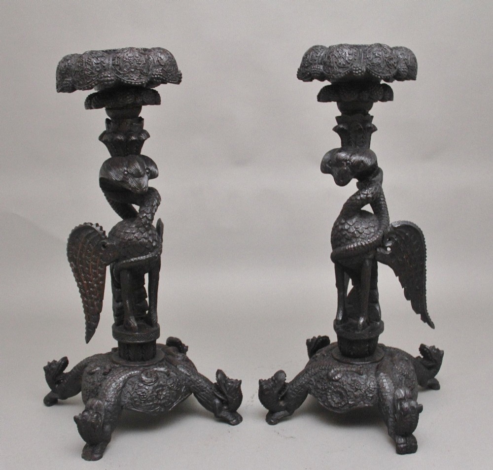 A pair of 19th-century Anglo-Indian carved hardwood torcheres featuring detailed cobra and mythical bird motifs topped with lotus platforms.