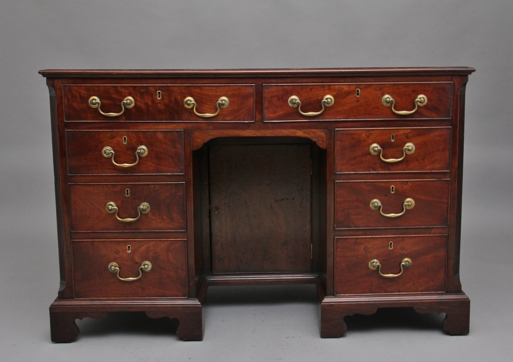 An 18th-century mahogany kneehole desk featuring a central recessed cupboard, multiple drawers with brass swan-neck handles, and bracket feet.