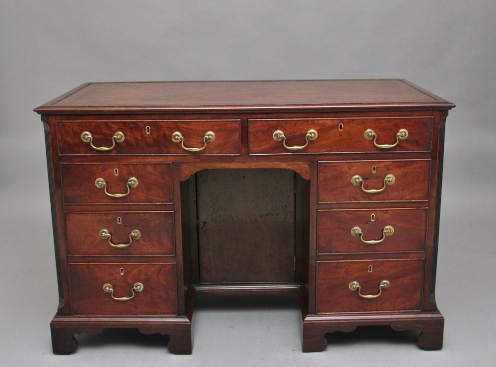 An 18th-century mahogany kneehole desk featuring a central recessed cupboard, multiple drawers with brass swan-neck handles, and bracket feet. View IV
