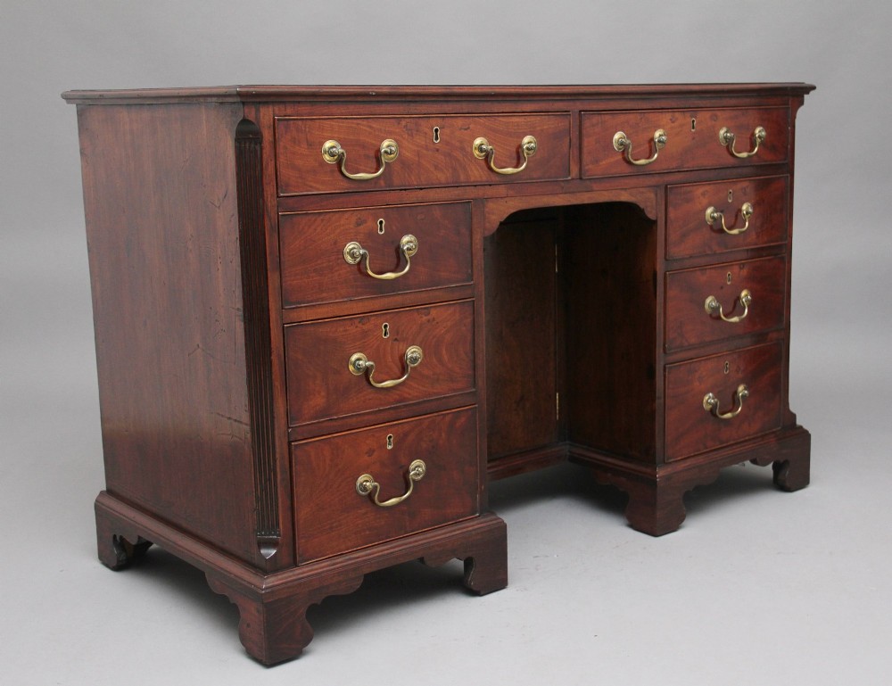 An 18th-century mahogany kneehole desk featuring a central recessed cupboard, multiple drawers with brass swan-neck handles, and bracket feet. View V