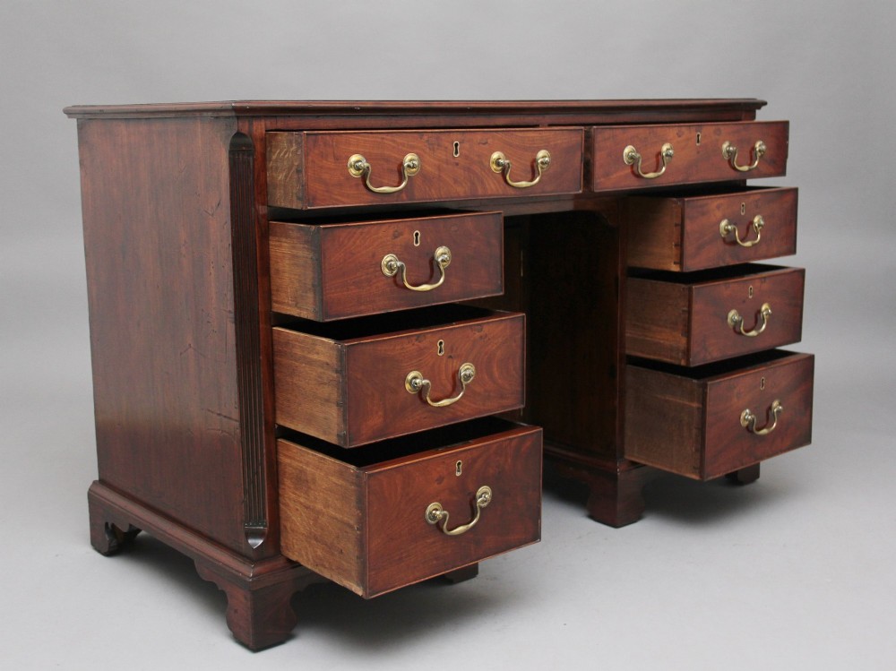 An 18th-century mahogany kneehole desk featuring a central recessed cupboard, multiple drawers with brass swan-neck handles, and bracket feet. View VI